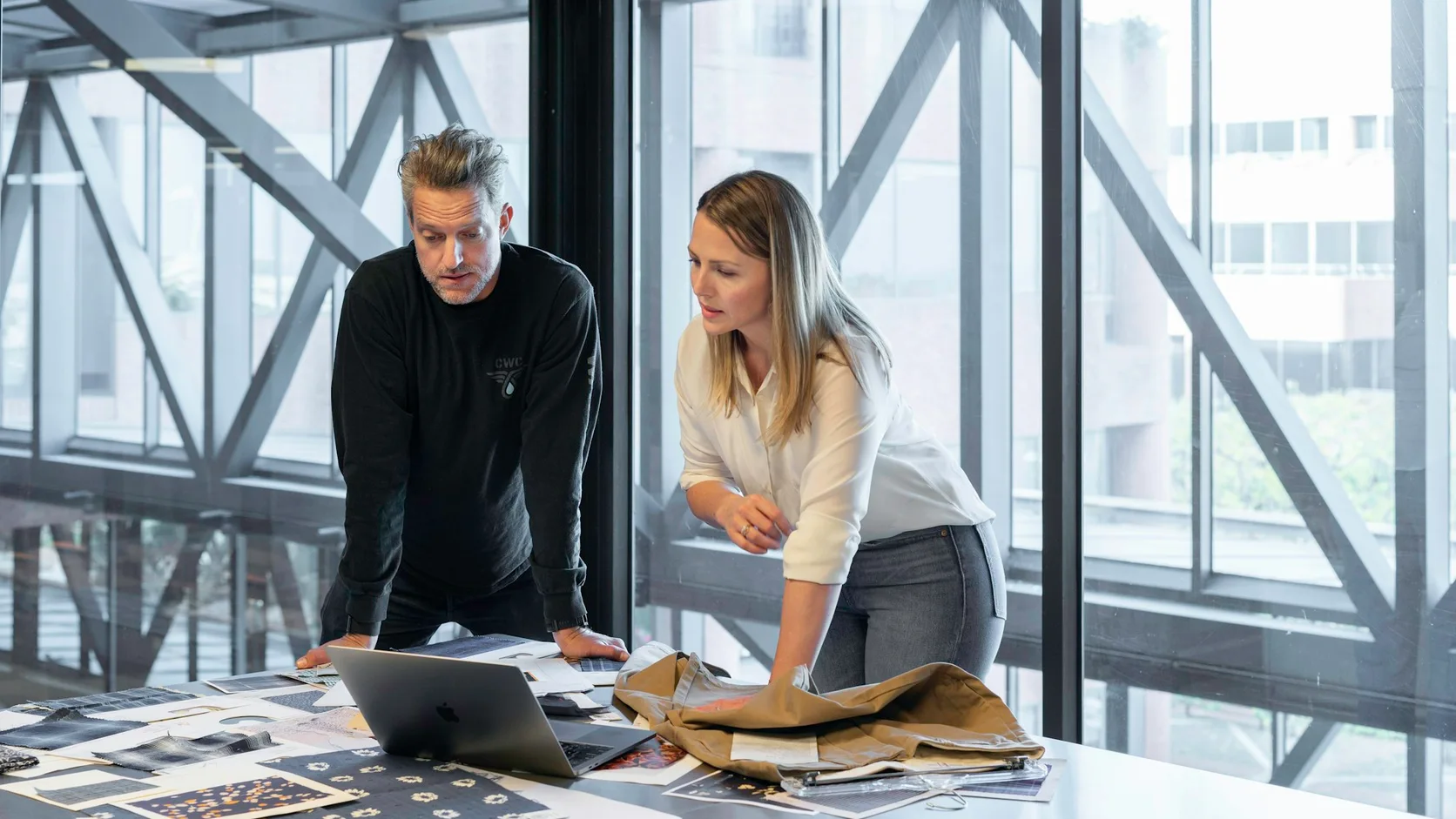 Zwei Personen besprechen Unterlagen und Materialmuster am Arbeitstisch.